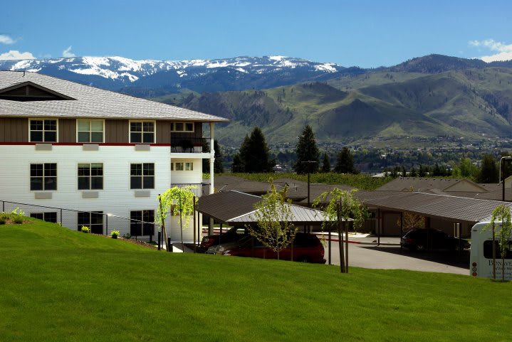 A scenic view of a building set against snow-capped mountains and lush green surroundings.