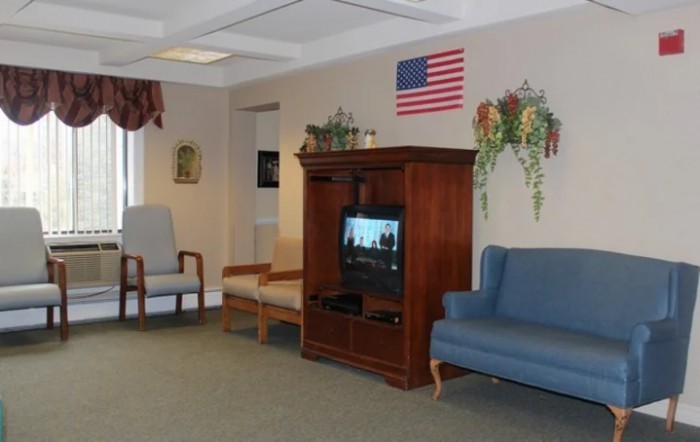 A waiting room with a television, chairs, and an American flag on the wall.