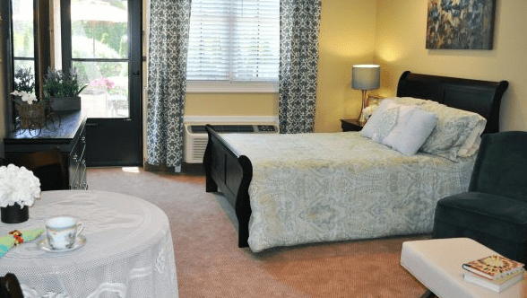 A cozy bedroom featuring a bed with a patterned bedspread, a lamp on a bedside table, and curtains framing a window.