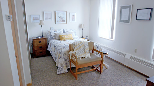 A cozy and well-decorated bedroom featuring a bed with floral bedding, a wooden chair, and soft natural light filtering through the window.