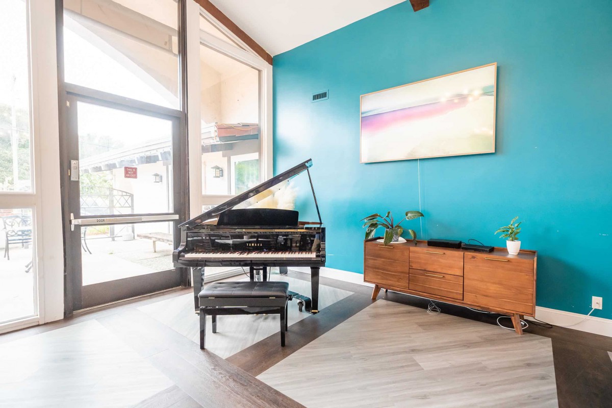 A stylish living room featuring a grand piano, turquoise accent wall, and mid-century modern furniture bathed in natural light.