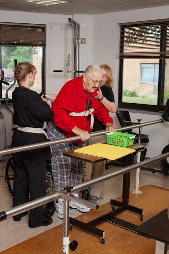 An elderly person receives assistance during a physical therapy session, supported by two caregivers.
