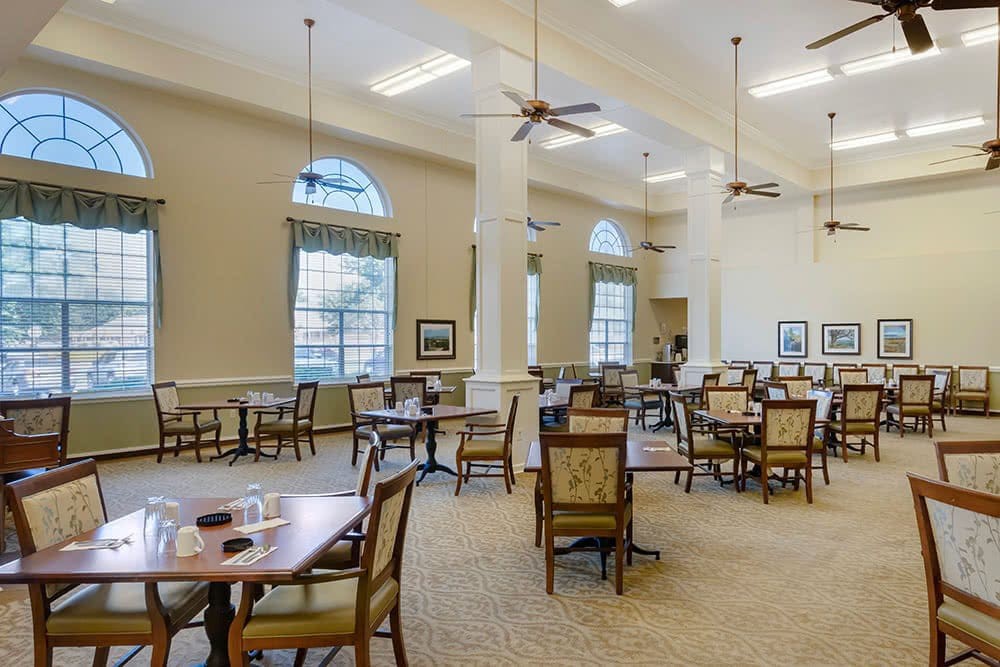 A spacious dining room with multiple tables and chairs, featuring high ceilings and large windows.