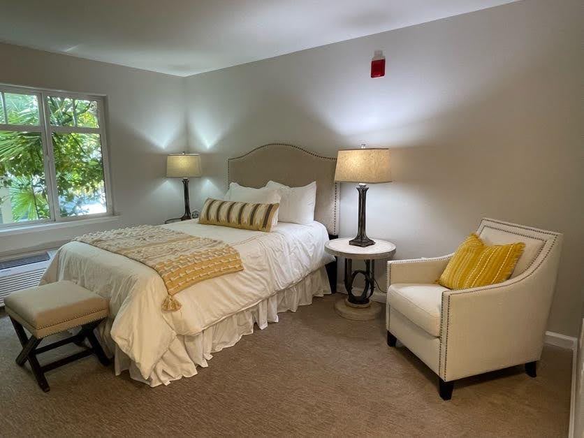 A cozy bedroom with neutral tones, featuring a comfortable bed, two bedside lamps, and an armchair.