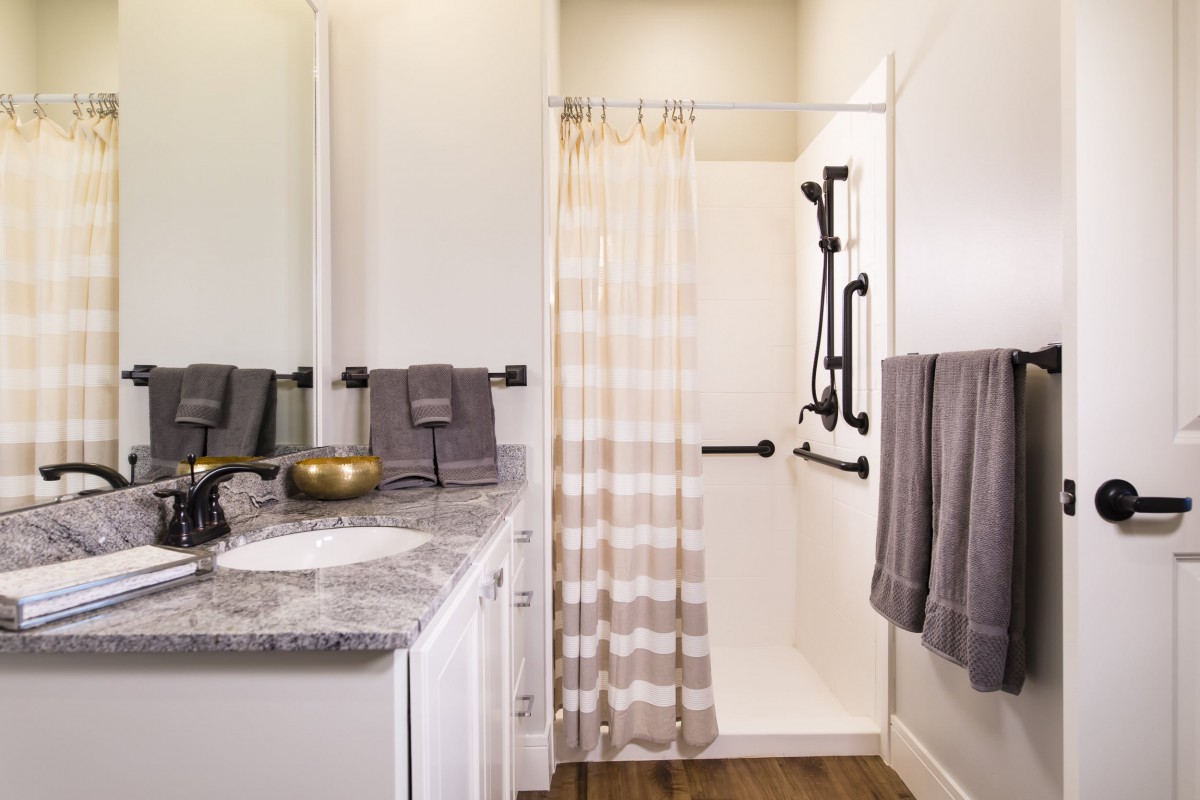 A modern bathroom with a shower area featuring grab bars and a striped curtain, alongside a sink and neatly arranged towels.