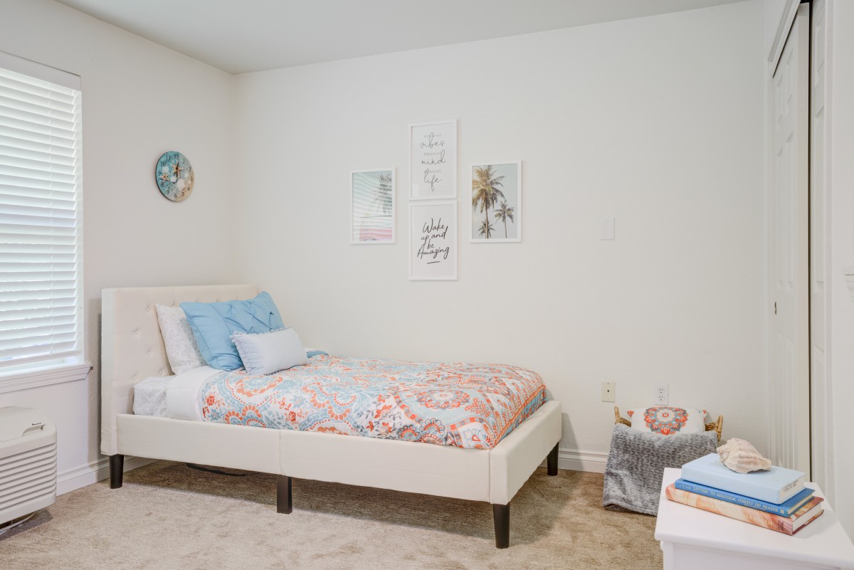 A minimalist bedroom featuring a neatly made bed with pastel bedding and simple wall decor.
