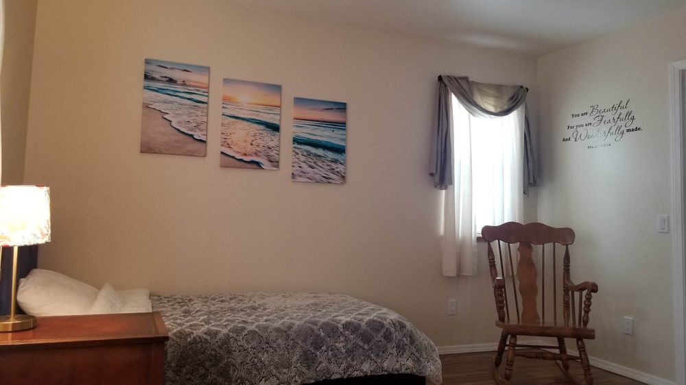 A cozy bedroom with ocean-themed artwork on the wall, a bed with patterned bedding, a window with curtains, and a wooden chair.