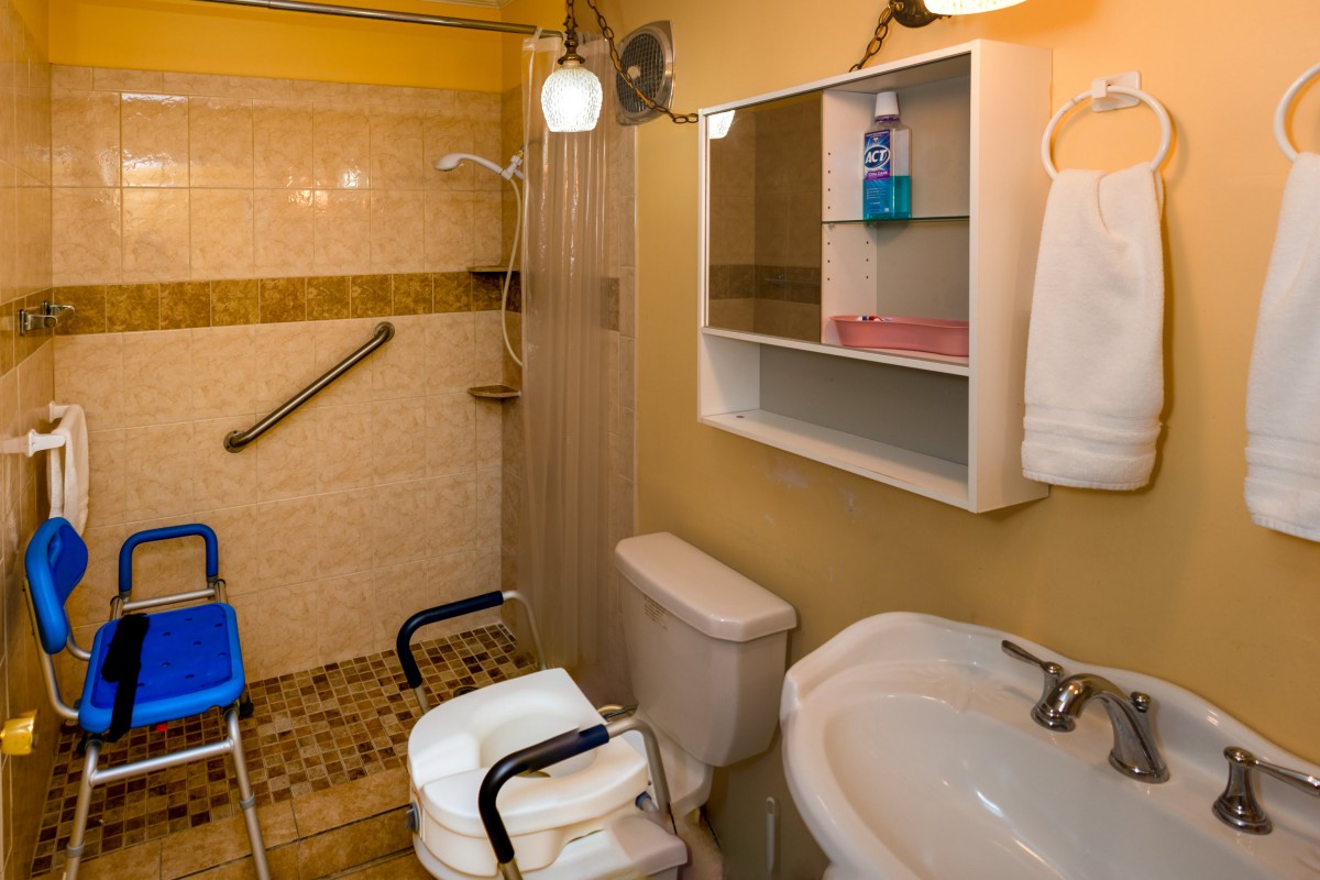 An accessible bathroom with a shower, toilet equipped with support handles, a sink and a mirror cabinet.