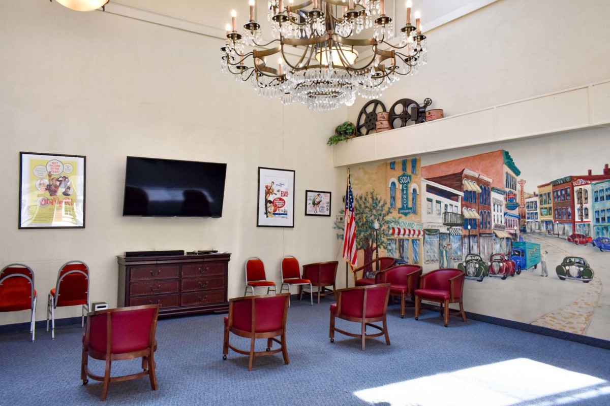 A spacious waiting area with red chairs, a mural on the wall, a large chandelier, and an American flag.