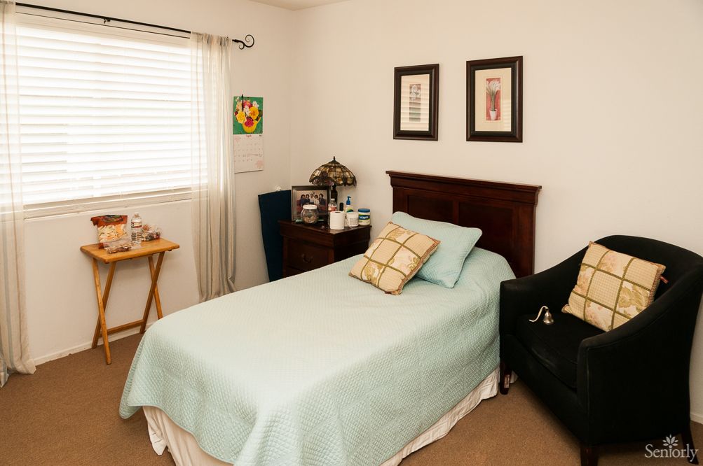 A cozy bedroom with a neatly made single bed, adorned with decorative pillows and artwork on the walls.