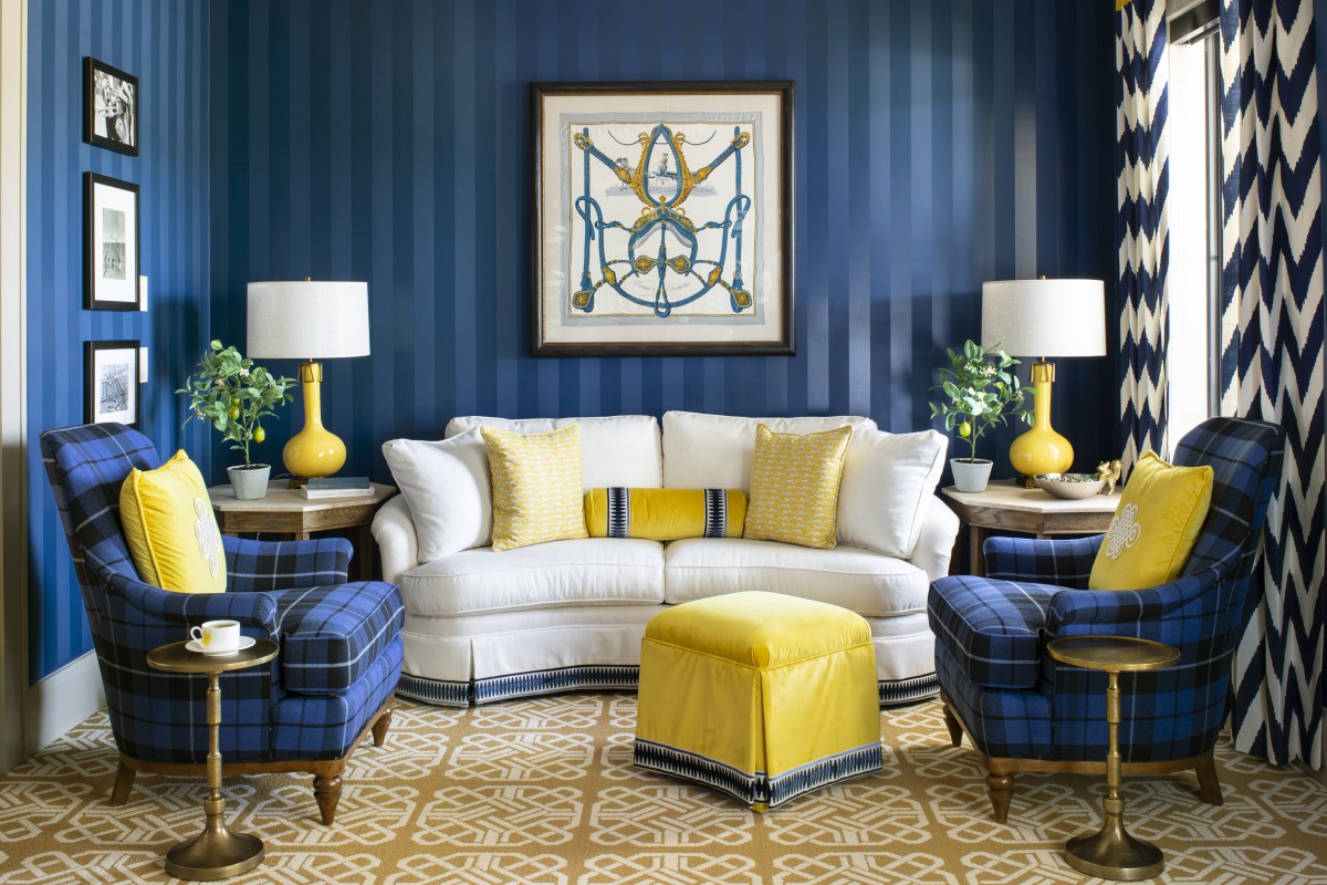 A stylish living room with blue walls and yellow accents, featuring a white sofa, plaid armchairs, and matching lamps.