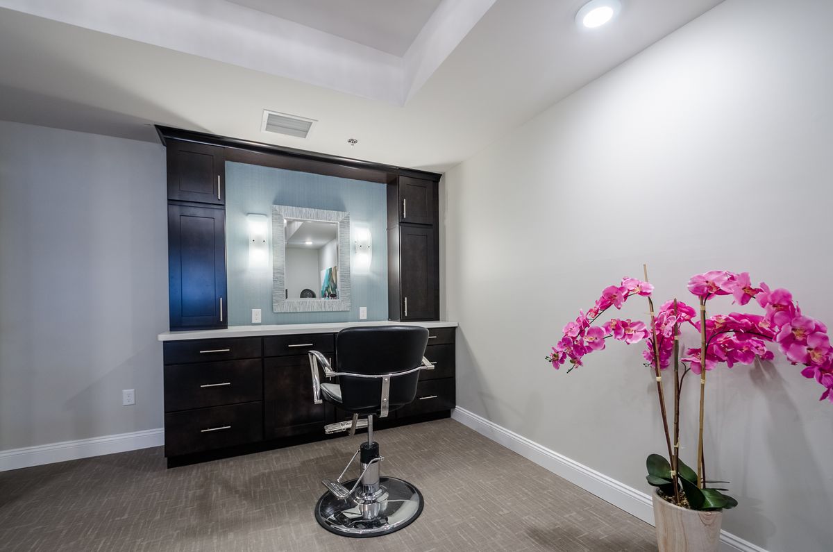 A modern vanity area with a chair, large mirror, and decorative flowers.