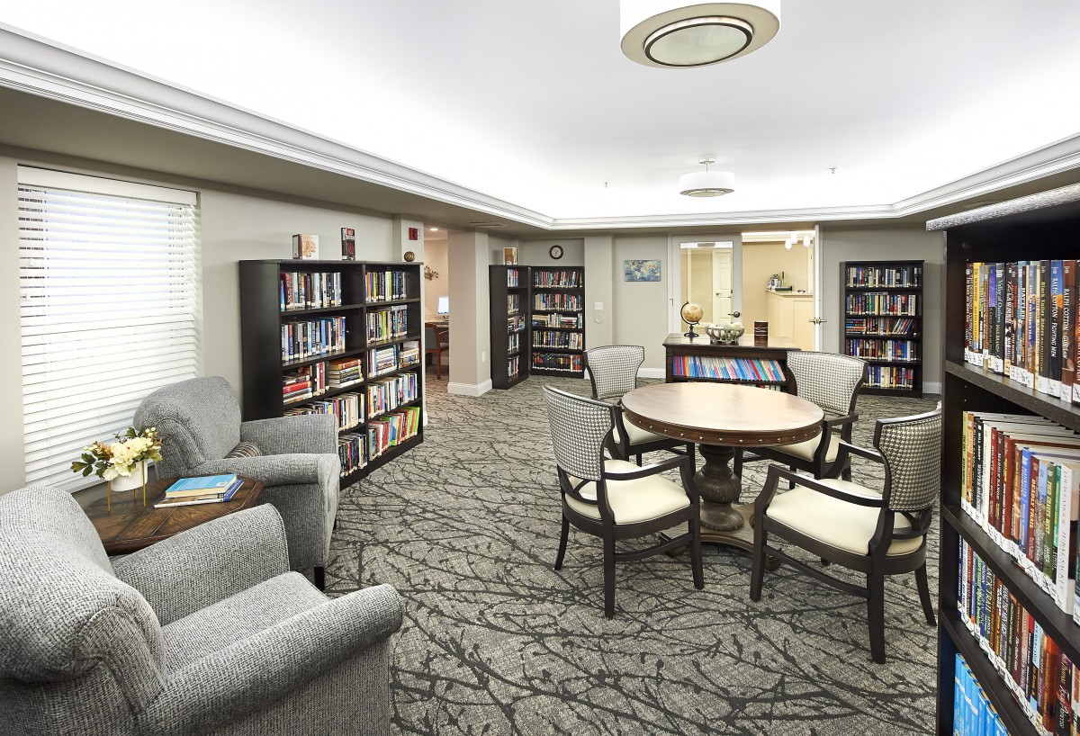 A cozy library area with bookshelves, a round table surrounded by chairs, and comfortable seating.