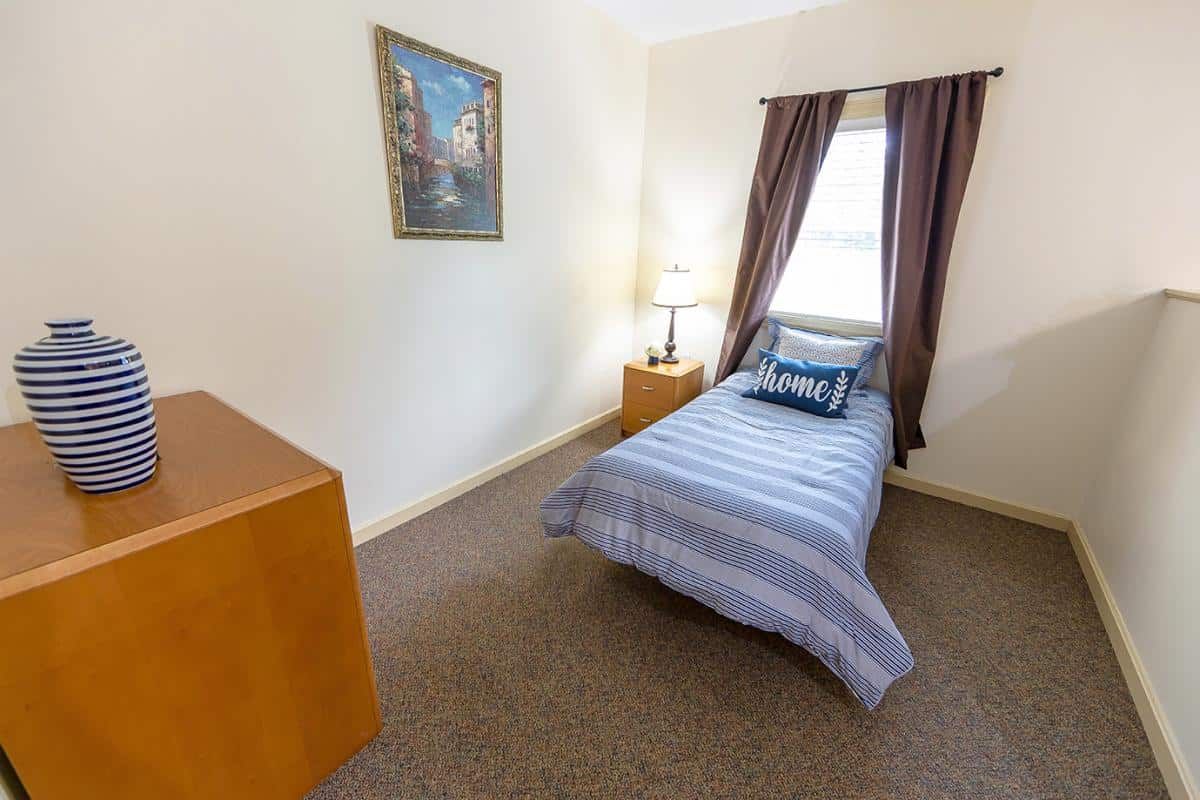 A cozy bedroom with a single bed, lamp, and window with curtains.