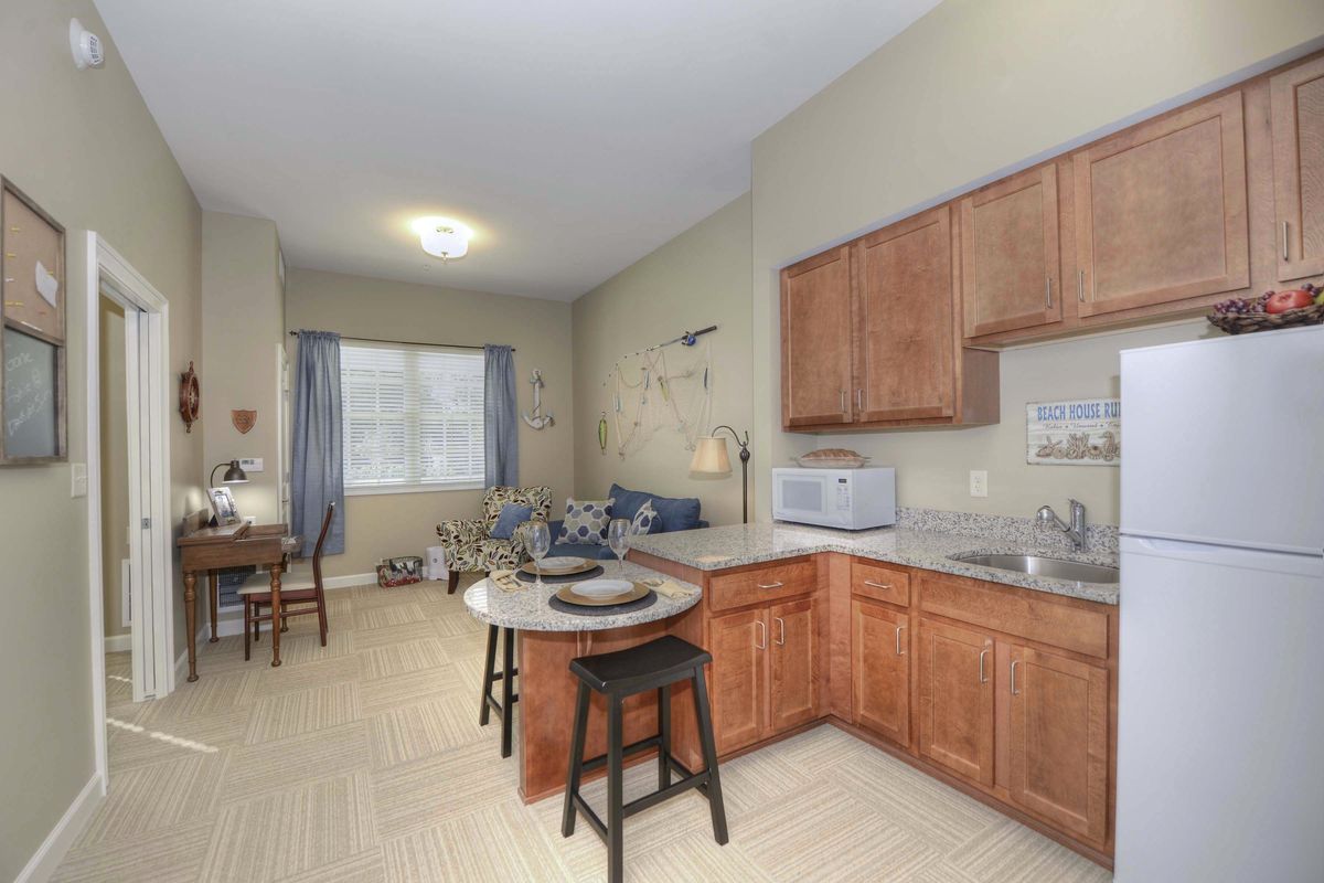 An open-plan apartment featuring a kitchen with wooden cabinets and bar stools, adjacent to a cozy living area.