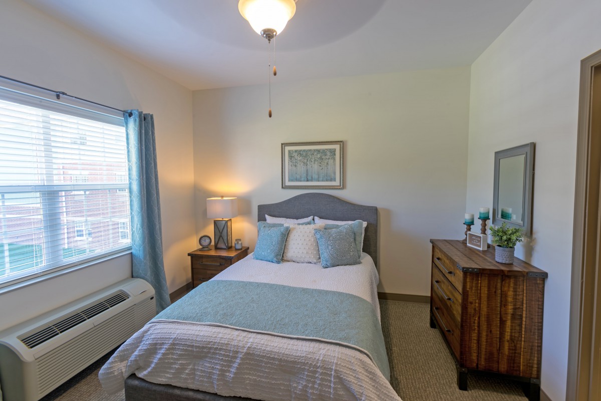 A cozy bedroom with a neatly made bed, bedside lamp, and decor.