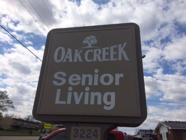 A sign for Oak Creek Senior Living against a cloudy sky.