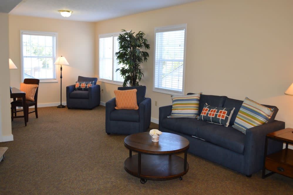 A cozy living room with blue sofas, a round coffee table, and natural lighting from multiple windows.