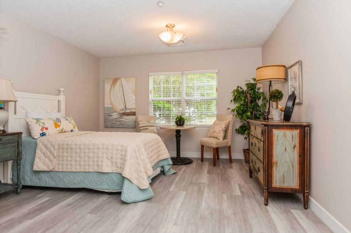 A cozy bedroom with a bed, dresser, and a window overlooking greenery.