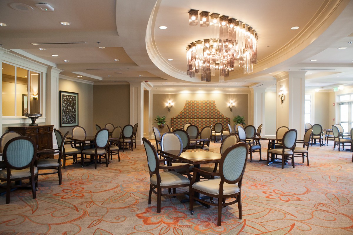 An elegant dining room with upholstered chairs, round tables, and a decorative chandelier.