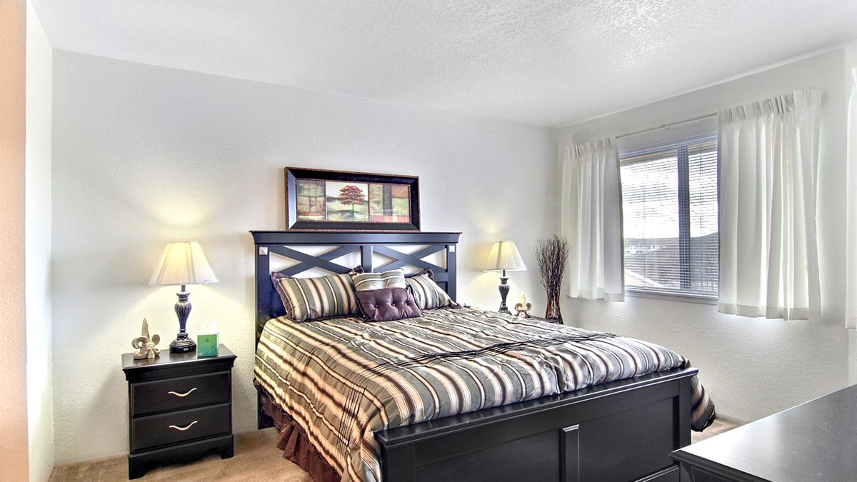 A cozy bedroom with a striped bedspread, wooden headboard, and two lamps.