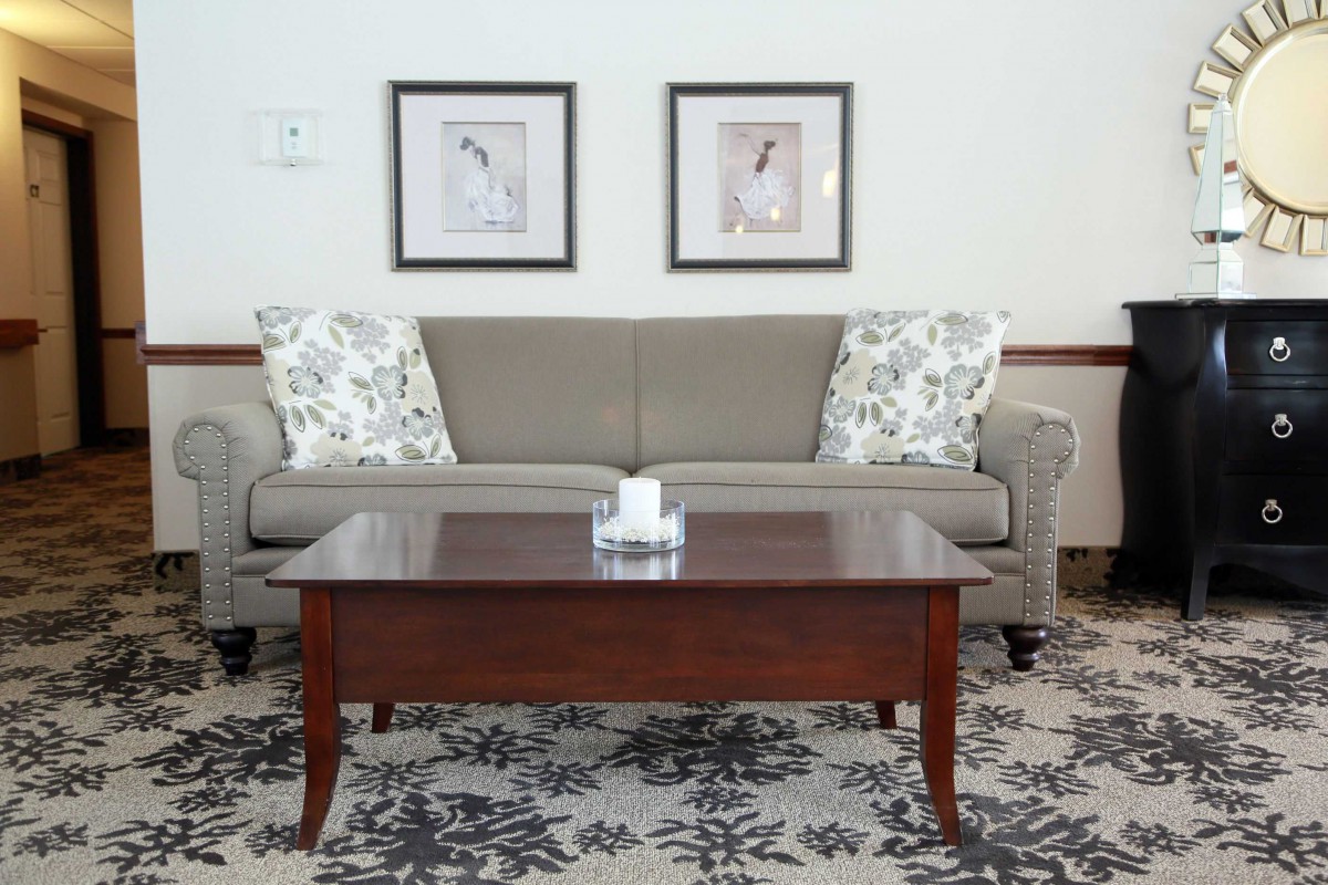 A cozy living room setup with a grey sofa, a wooden coffee table, floral cushions, and framed artwork on the wall.