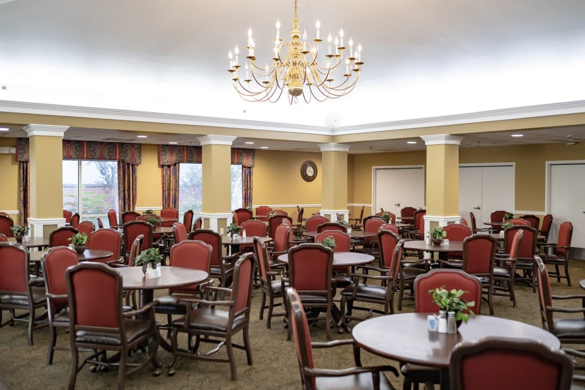An elegant dining room with multiple tables and chairs, highlighted by a large chandelier.