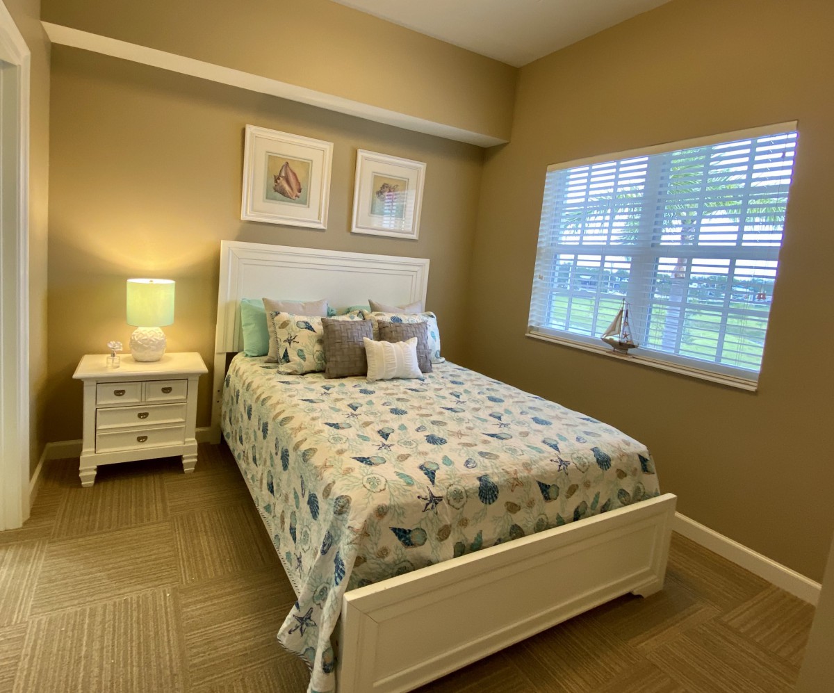 A cozy bedroom with a neatly made bed, nightstand, and lamp by the window.