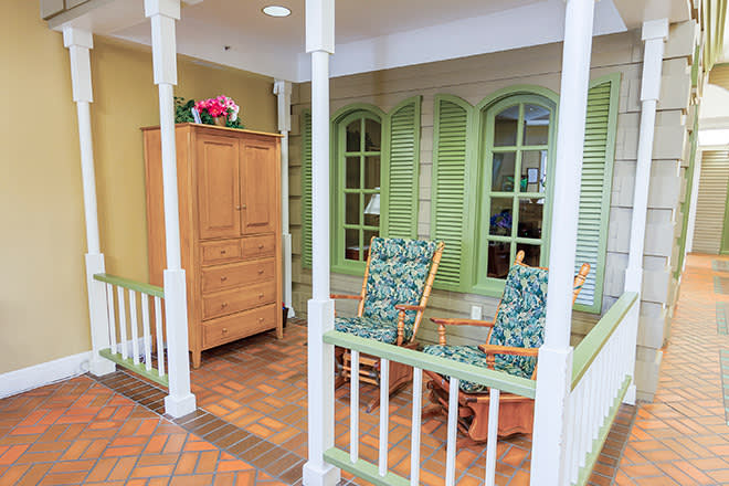 A cozy porch with green shuttered windows, wooden rocking chairs, and a cabinet adorned with flowers.