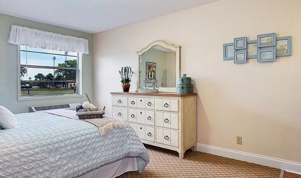 A cozy bedroom featuring a dresser with a mirror, bed, and window allowing natural light.