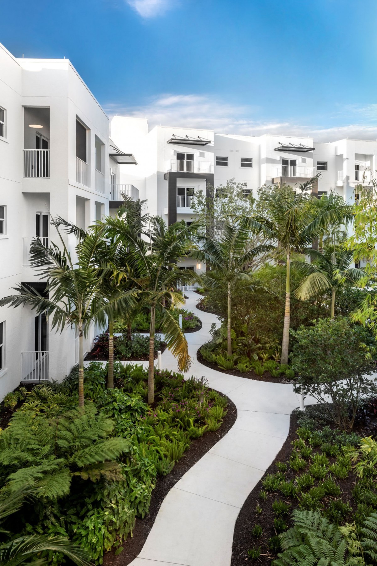 Modern apartment complex with tropical landscaping and winding pathways.