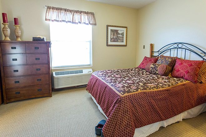 A cozy bedroom featuring a bed with patterned bedding, a dresser, and a window with curtains.