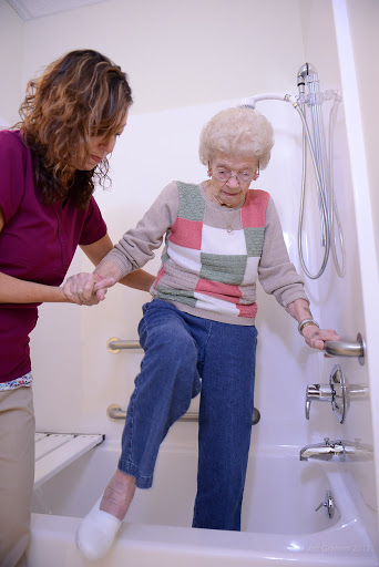 A caregiver helps an elderly woman safely enter the shower.