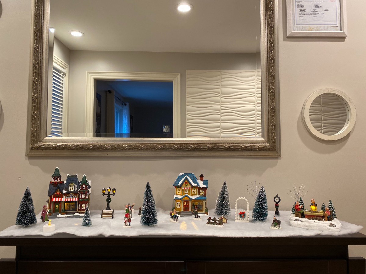 A charming miniature holiday village displayed on a shelf with a large mirror reflecting the scene.