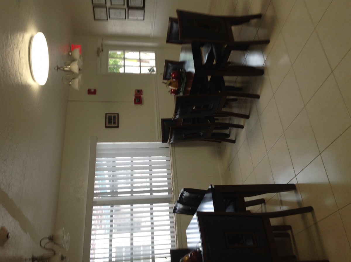 A well-lit dining room featuring a wooden dining set with chairs and large windows.