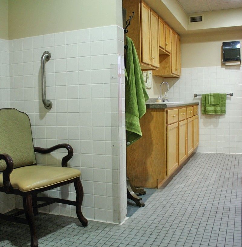 A combined kitchen and bathroom area with wooden cabinets, a tiled floor, and green towels.