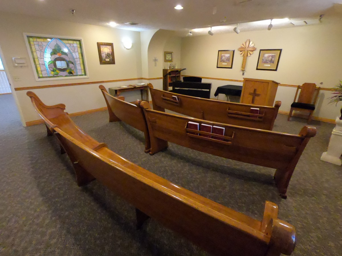 A small chapel interior with wooden pews, an altar, and a cross on the wall.