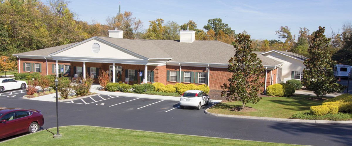 A suburban building with a brick exterior and an adjacent parking lot containing a white car.