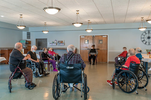 A group of elderly individuals in wheelchairs gathered together in a care facility, engaging in a social activity.