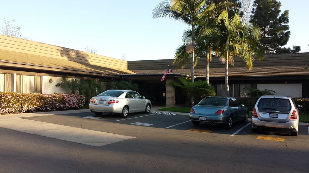 A small parking lot with two cars in front of a building surrounded by palm trees on a sunny day.