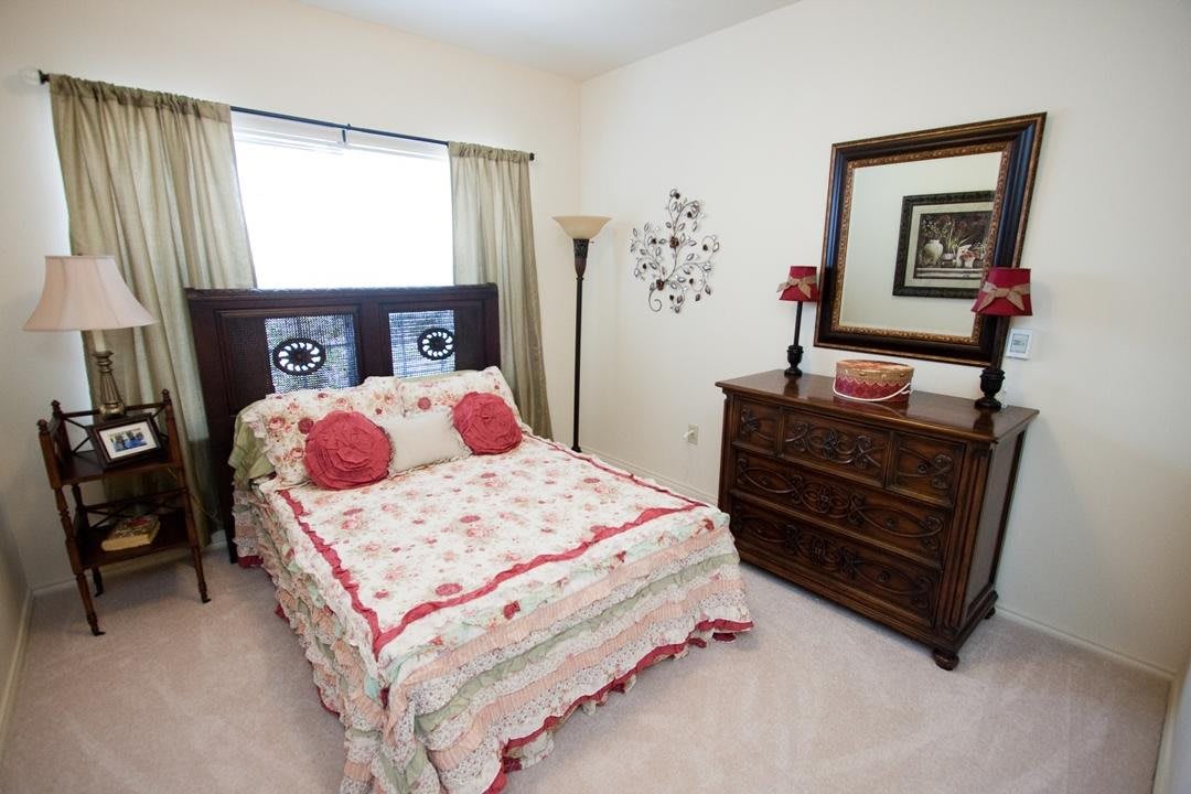 A cozy bedroom with floral bedding, a wooden dresser, and a large mirror.