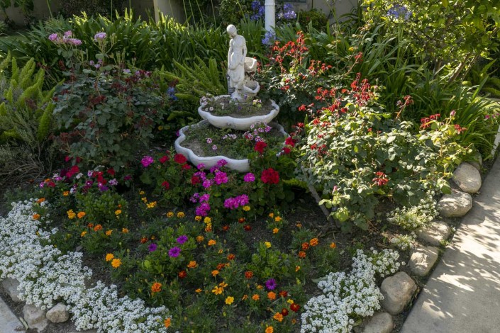 A beautiful garden scene featuring a small fountain with a statue surrounded by vibrant flowers and lush greenery.