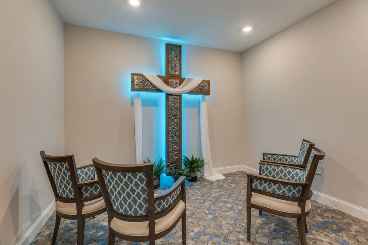 A small chapel interior featuring a prominent cross with decorative lighting and arranged chairs.
