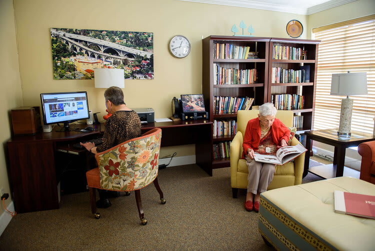 An elderly man using a computer and an elderly woman reading in a cozy library setting.