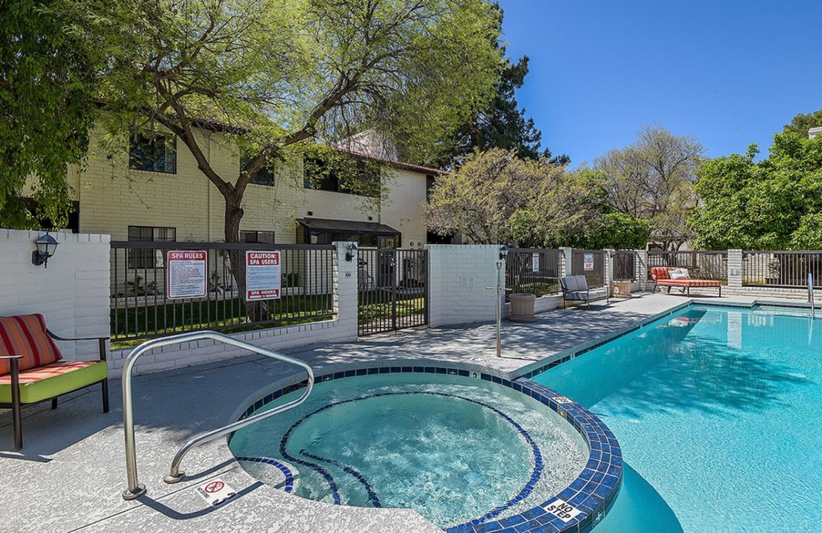 An outdoor pool area with a hot tub next to an apartment building on a sunny day.
