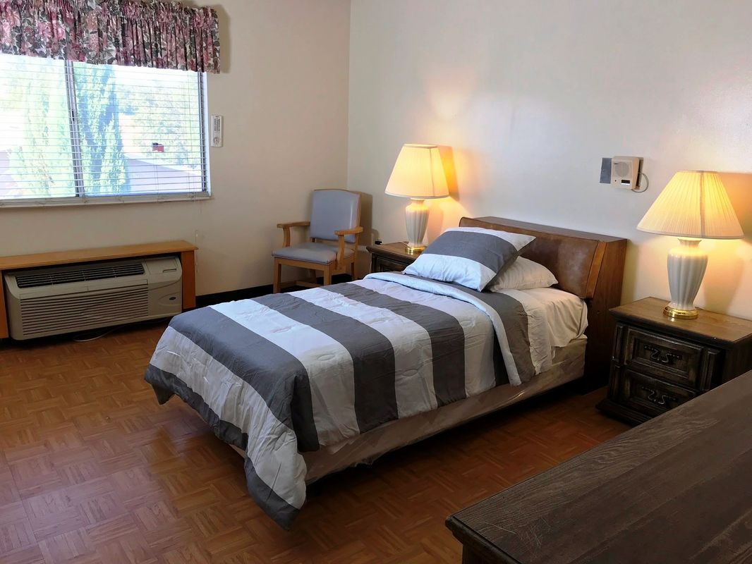 A minimalist bedroom featuring a single bed with striped bedding, a cozy chair by the window, and warm lighting from a bedside lamp.