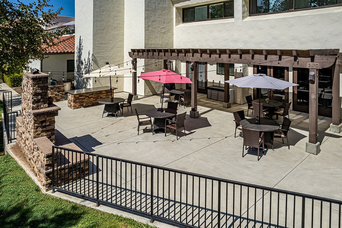 A spacious outdoor patio with tables, chairs, and umbrellas under a pergola.