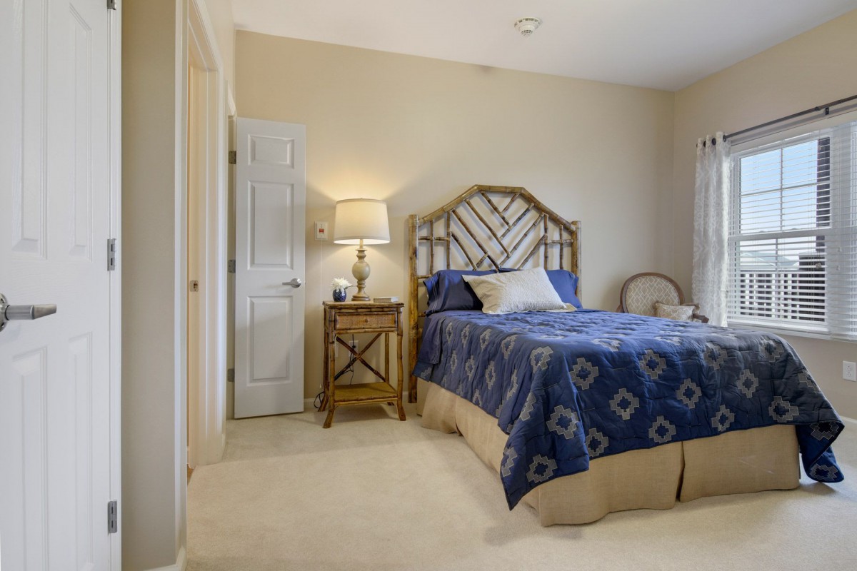 A cozy bedroom with a blue-patterned bed, nightstand, and lamp.