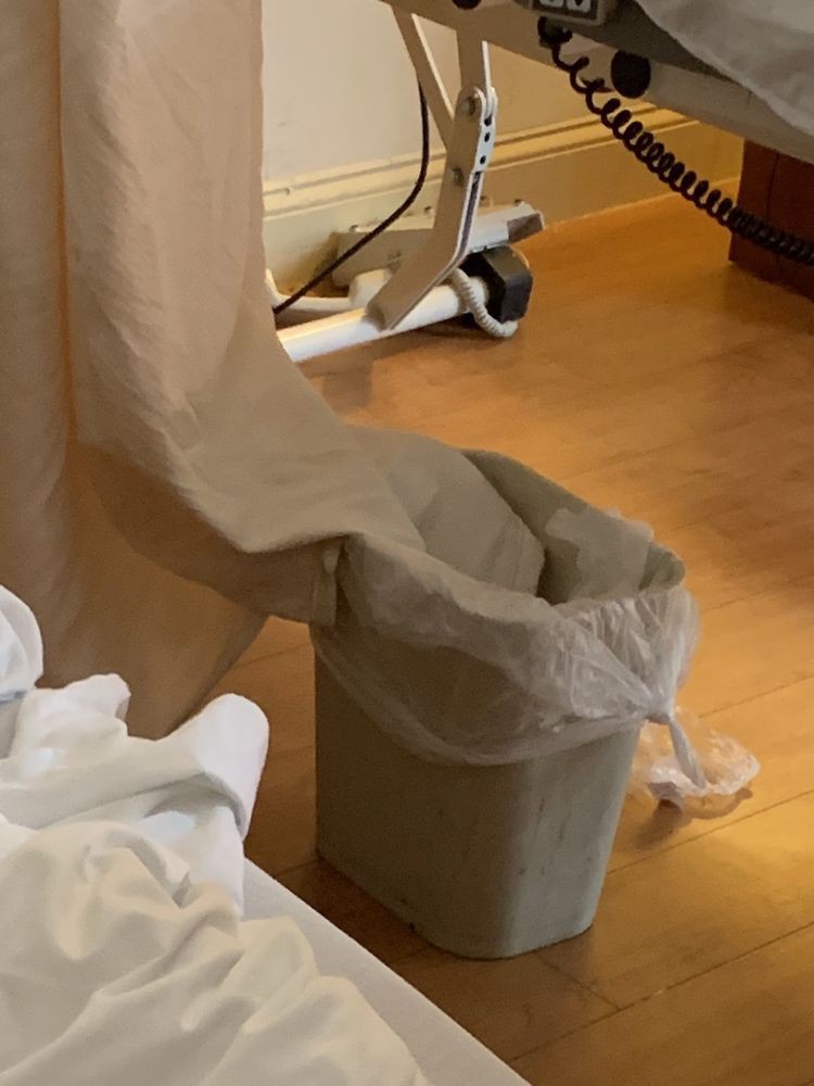 A trash can with a plastic liner situated indoors on a wooden floor.