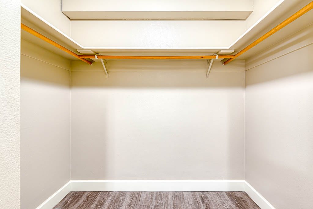 An empty walk-in closet with wooden rods and white walls.